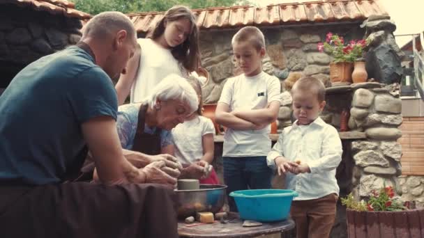 Бабушка и дедушка с внуками делают кувшин в керамике — стоковое видео