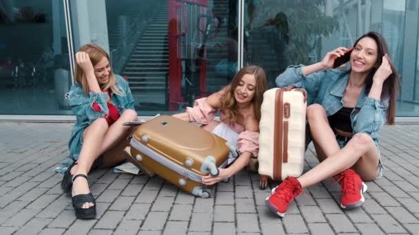 Meninas felizes sentadas perto do aeroporto com bagagem — Vídeo de Stock