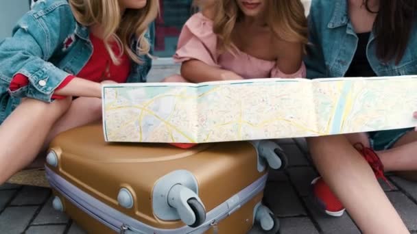 Девушки смотрят на карту, сидя с рюкзаком возле аэропорта — стоковое видео