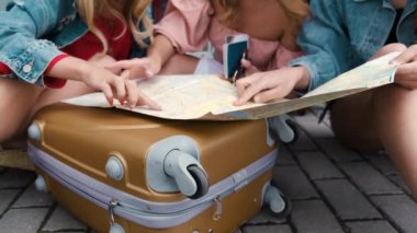 Havaalanı yakınında bagajla oturan haritaya bakan kızlar