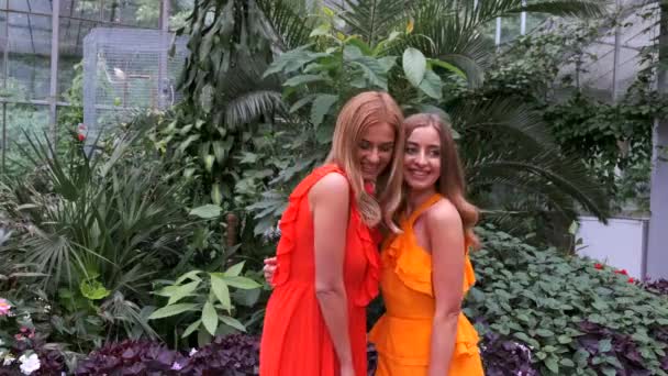 Дві дівчини в яскравих сукнях позує в ботанічному саду — стокове відео