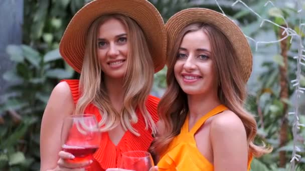 Портрет дівчат у капелюхах, що тримають келихи вина в ботанічному саду — стокове відео