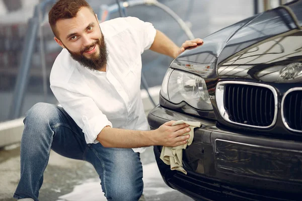 Un hombre con una camisa blanca limpia un auto en un lavado de autos —  Fotos de Stock