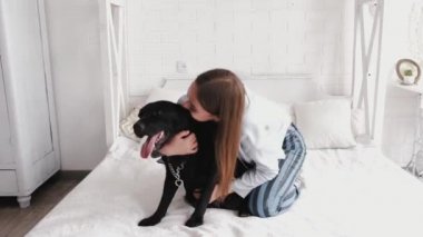 brunette kissing labrador dog sitting on bed in white room