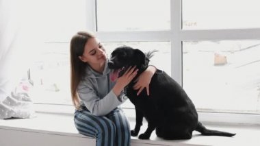 Pencerenin kenarında oturan kız siyah bir labradorla oynuyor.