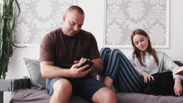 Padres con hija vestida con ropa casual en casa relajándose en el sofá con el perro — Vídeo de stock