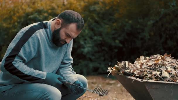 Gartenarbeiter, der ein Mann ist, der die trockenen Blätter von der Harke entfernt und reinigt — Stockvideo