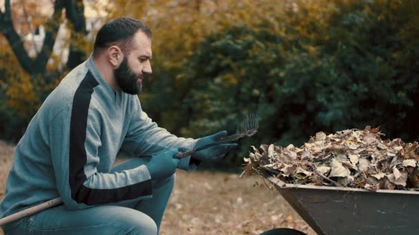 Gartenarbeiter, der ein Mann ist, der die trockenen Blätter von der Harke entfernt und reinigt — Stockvideo