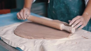 Bir kadın çömlekçi önlük giyip çamur hazırlıyor.