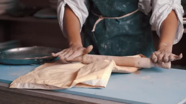 Een vrouw pottenbakker dragen een schort bereiden en rollen klei met een rollingpin — Stockvideo