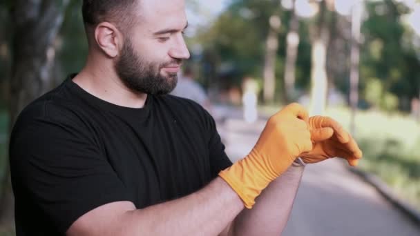 Мужчина снимает резиновые перчатки после окончания волонтерской работы в местном парке — стоковое видео