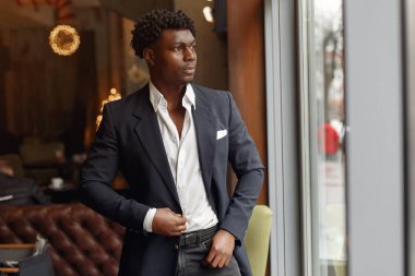 Siyah takım elbiseli siyah bir adam bir kafede duruyor.