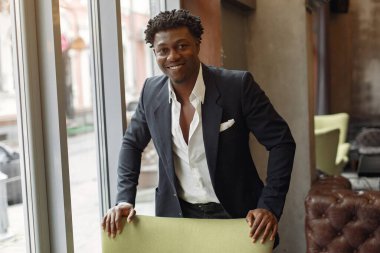 Siyah takım elbiseli siyah bir adam bir kafede duruyor.