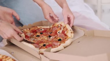 Kadın ellerine yakın çekim, pizzadan bir dilim alıyor.