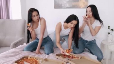 Üç kız arkadaş yatakta pizza yiyor ve eğleniyorlar.