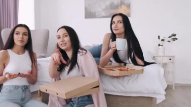 Güzel bayanlar yatak odasında pizza yiyor ve gülümsüyor.