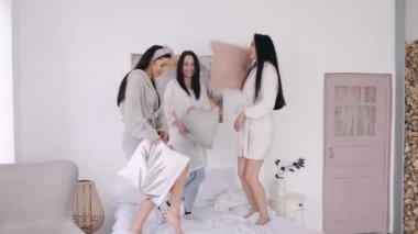 Güzel bayan arkadaşlar yataklarında yastıklarla oynuyorlar.