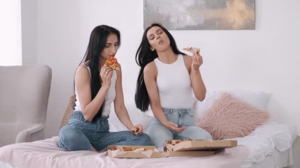 Två vackra kvinnor äter pizza i sovrummet. — Stockvideo