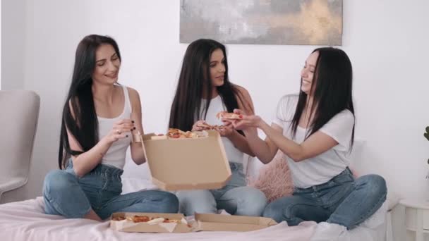 Drie mooie voortekenen eten afhaalpizza in de slaapkamer. — Stockvideo