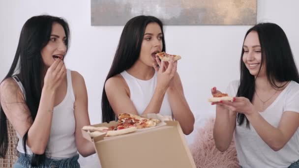 Tre vackra omen äter pizza i sovrummet. — Stockvideo