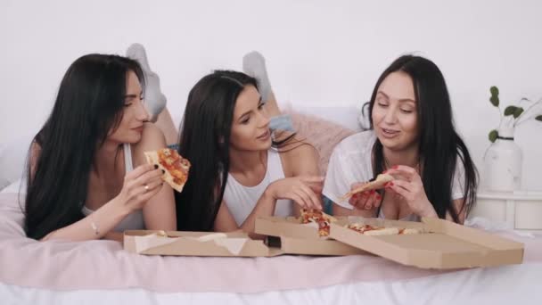 Tres hermosas novias están tumbadas en la cama y comiendo pizza a domicilio — Vídeos de Stock