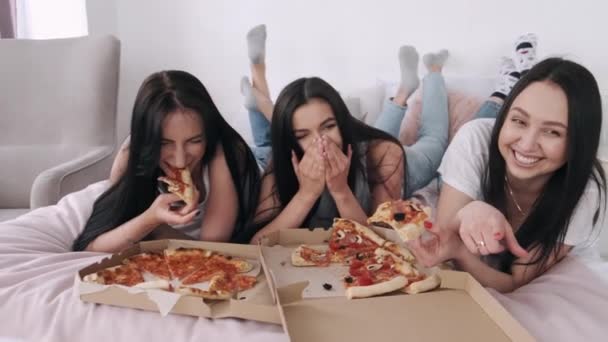 Drei hinreißende Freundinnen liegen auf dem Bett und essen Pizza — Stockvideo