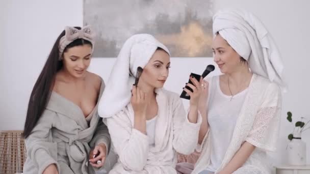 Piękne młode kobiety w szatach i włosach owinięte w ręczniki robią makijaż — Wideo stockowe
