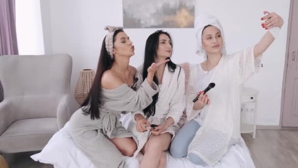 Три красиві подружки беруть селфі і роблять макіяж у спальні — стокове відео