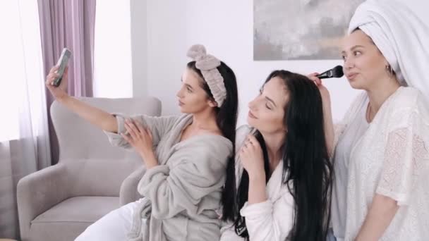 Three pretty girlfriends are taking selfies and doing makeup in a bedroom — Stock Video