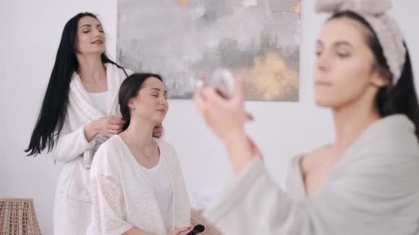 Egy közeli kép egy gyönyörű nőről, aki sminkeli magát, és két lány van mögötte. — Stock videók