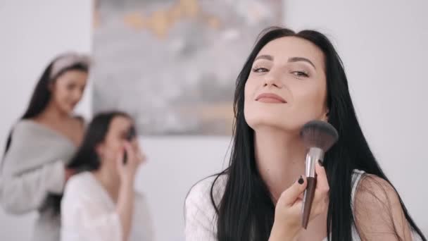 Una vista cercana de una hermosa mujer haciendo su maquillaje y dos chicas detrás — Vídeos de Stock