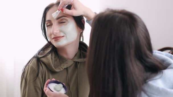 A mulher está a aplicar uma máscara facial no rosto dos amigos. — Vídeo de Stock