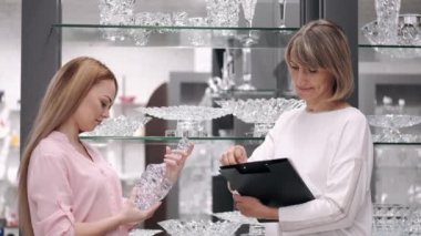 Kadın bir tezgahtarla cam eşyalar seçiyor.