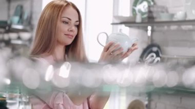 Genç bayan yemek malzemeleri dükkanındaki cam çaydanlığa bakıyor.