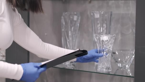 The serious woman in mask is checking the glassware in a shop — Stock Video