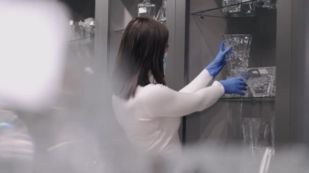 La femme sérieuse masquée vérifie la verrerie dans un magasin — Video