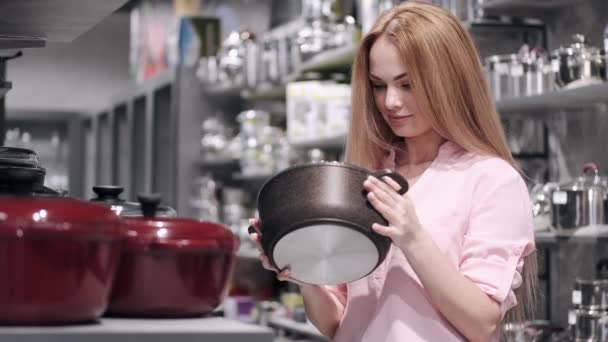 La mujer bonita está eligiendo una sartén en una tienda de vajilla — Vídeos de Stock