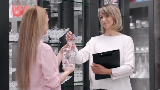 A mulher está escolhendo copos com um assistente de vendas uma loja de utensílios de mesa — Vídeo de Stock