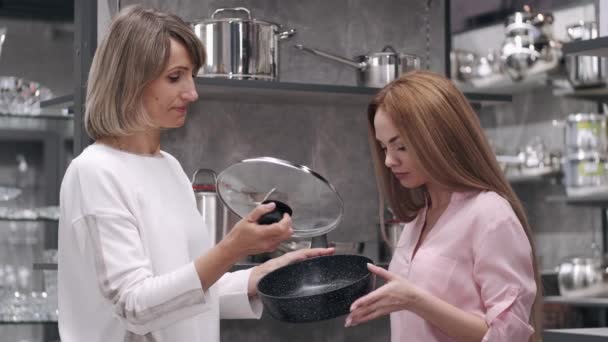 De aantrekkelijke vrouw en verkoopster controleren de pan in de servies winkel — Stockvideo