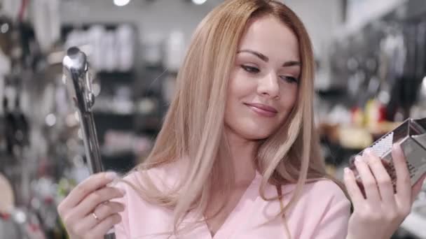 La hermosa mujer sostiene un rallador y pinzas culinarias en la tienda — Vídeo de stock