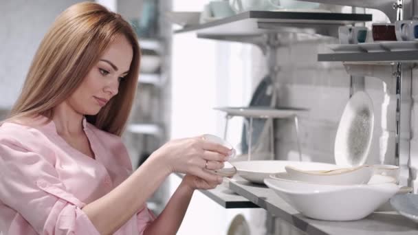 La bonita ama de casa está eligiendo vajilla de porcelana en la tienda de utensilios de cocina — Vídeos de Stock