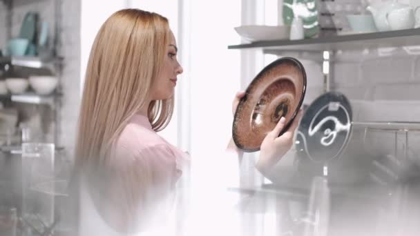 La joven está mirando el plato de cerámica en la tienda — Vídeos de Stock