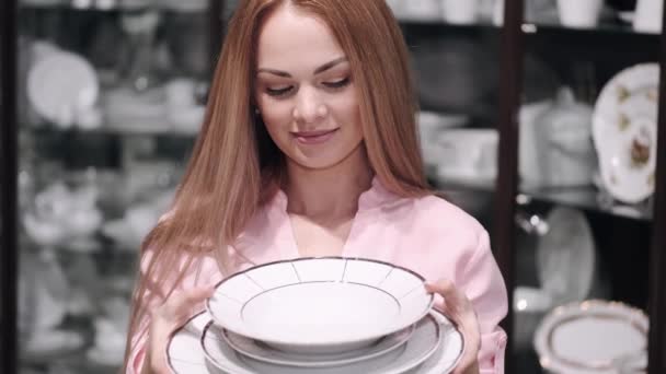 Красивая молодая женщина выбирает набор фарфоровых тарелок — стоковое видео