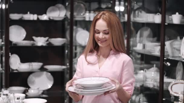 La hermosa joven está eligiendo un conjunto de platos de porcelana — Vídeo de stock