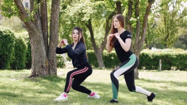 Twee jonge dames zitten te hurken in het park. — Stockvideo