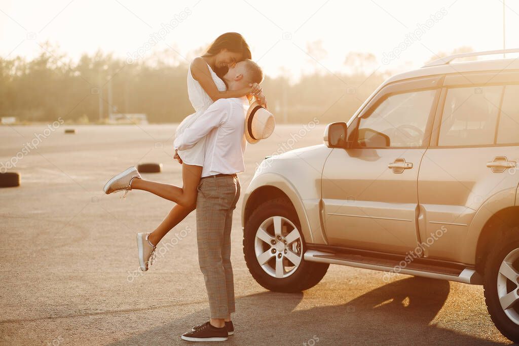 Beautiful couple spend time in a summer park near a car