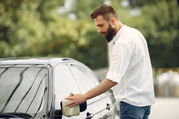 Мужчина в белой рубашке вытирает машину в автомойке — стоковое фото
