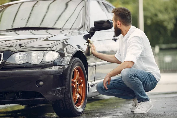 흰색 셔츠를 입은 남자가 세차를 하면서 차를 닦는다 — 스톡 사진