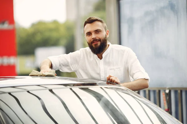 Un hombre con una camisa blanca limpia un auto en un lavado de autos —  Fotos de Stock