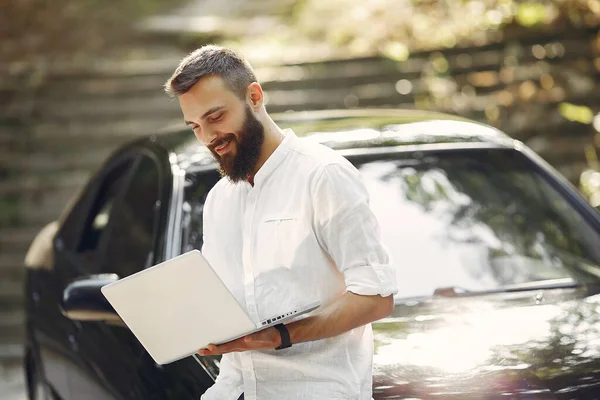Стильный бизнесмен, стоящий рядом с машиной и пользующийся ноутбуком — стоковое фото